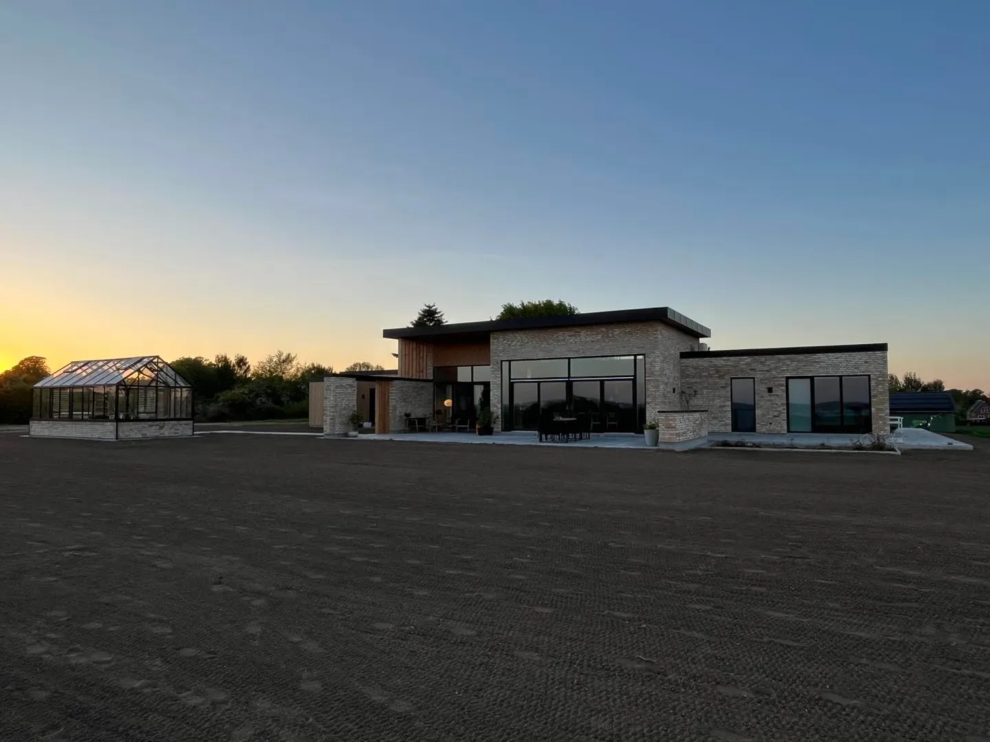 Nybygget hus i lyse mursten med store vinduespartier og drivhus, fotograferet ved solnedgang