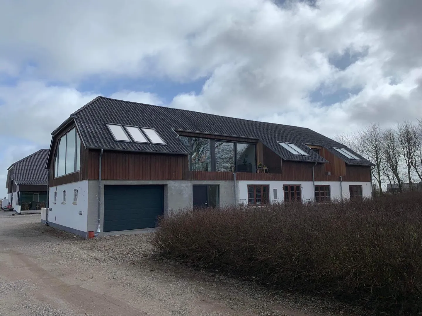 Ombygget landbrugsbygning med træbeklædt førstesal, ovenlysvinduer og stort vinduesparti