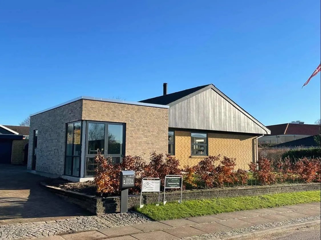 Hus i gule mursten med ny tilbygning i grå mursten og hjørnevinduer